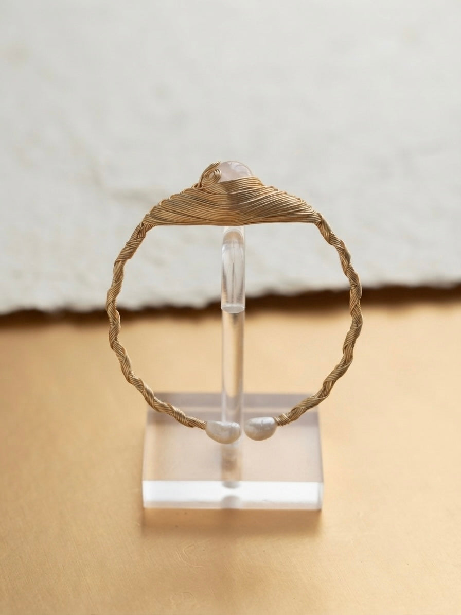 Twisted gold wire pearl cuff on a clear display stand