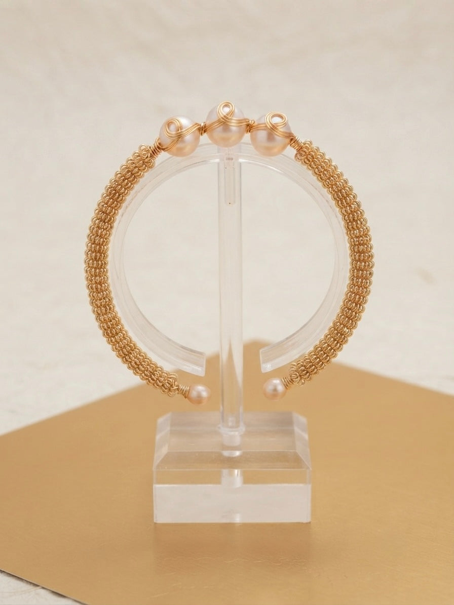 Woven gold triple pearl cuff on a clear display stand