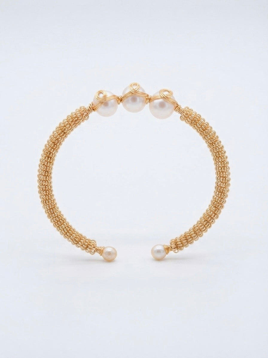 Woven gold triple pearl cuff on a white background