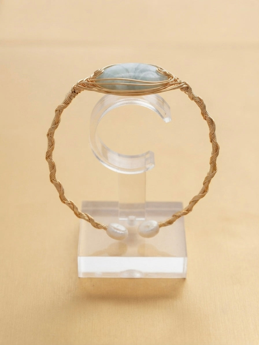 Twisted gold wire cuff with blue-grey stone on a clear display stand
