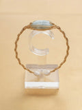 Twisted gold wire cuff with blue-grey stone on a clear display stand