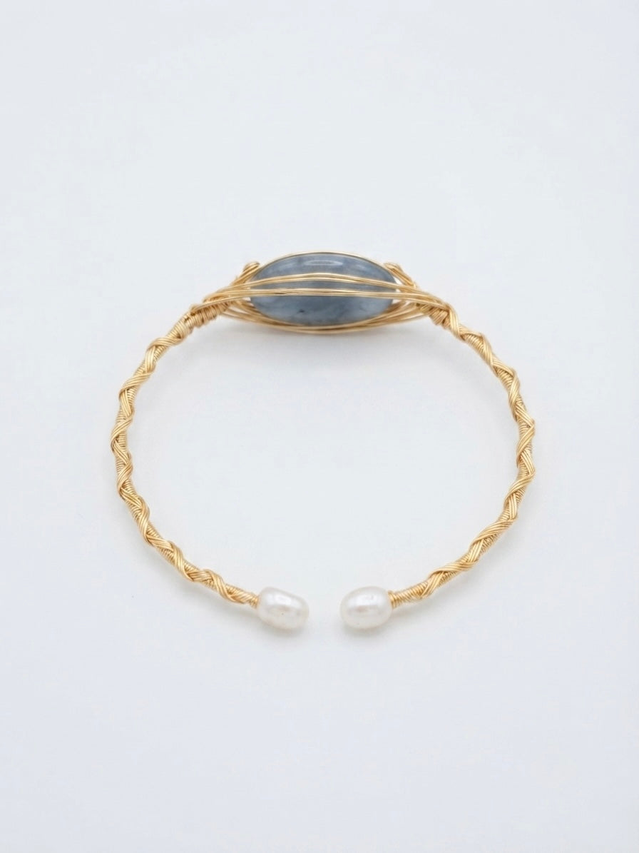 Twisted gold wire cuff with blue-grey stone and pearl ends on a white background