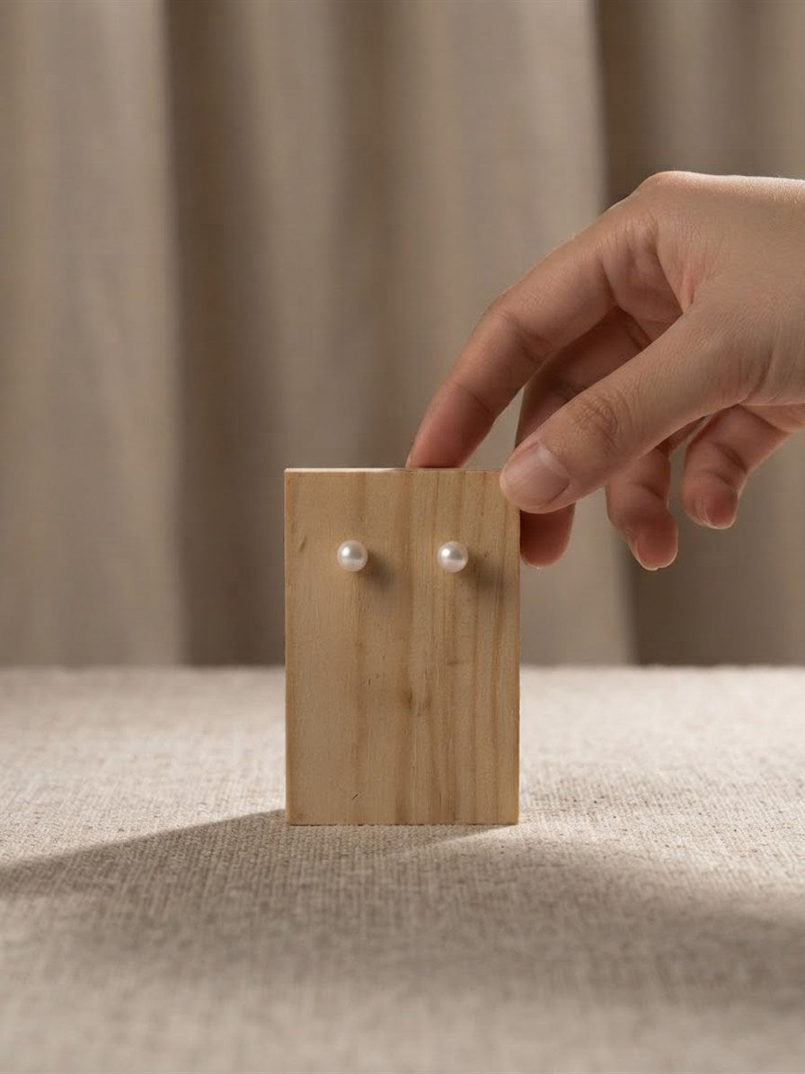 Akoya pearl stud earrings displayed on a wooden stand