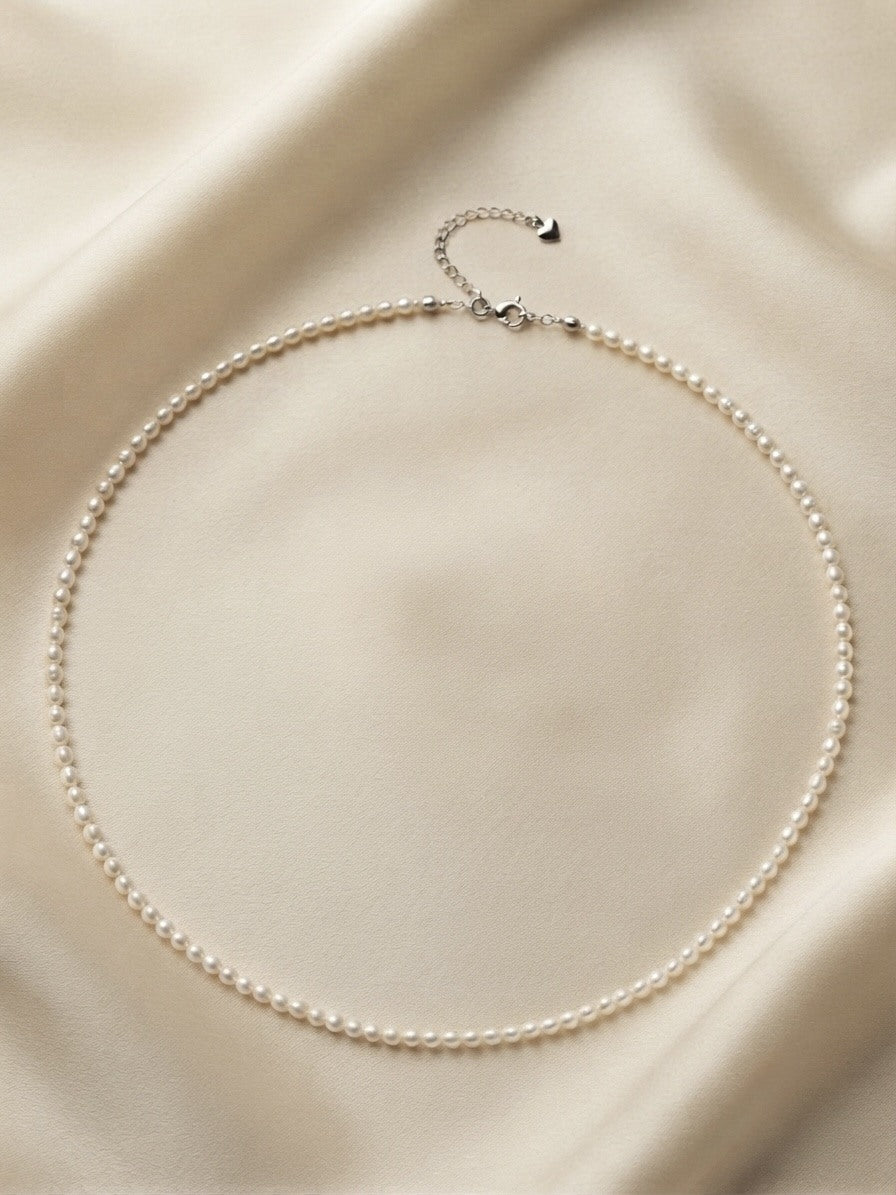 Freshwater baby pearl necklace laid on ivory silk