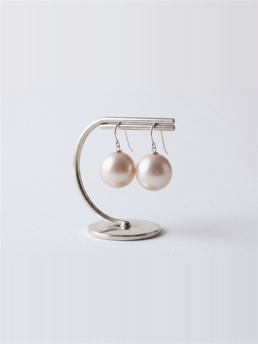 Large pearl drop earrings hanging on a silver display stand