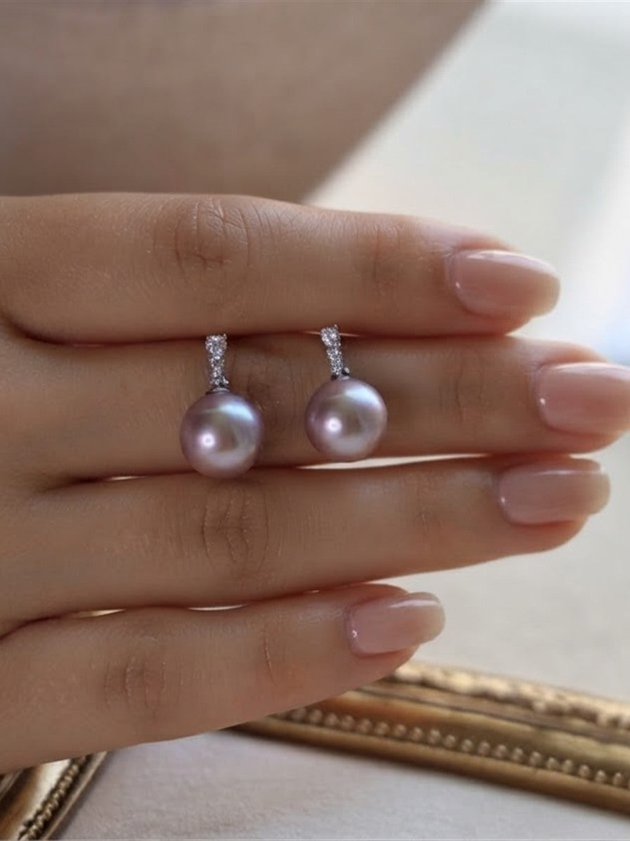 Lavender pearl drop earrings held between the fingers