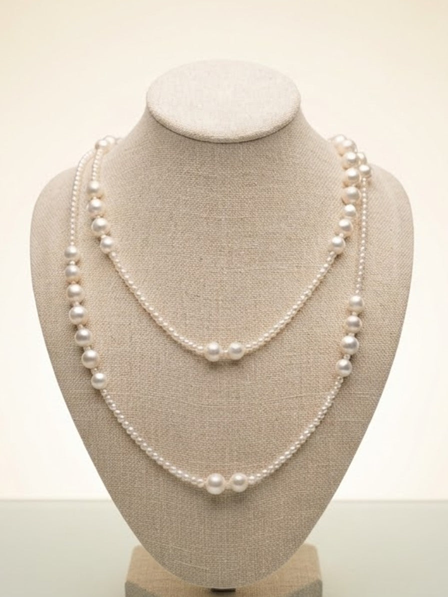 Long freshwater pearl necklace worn doubled on a linen display bust