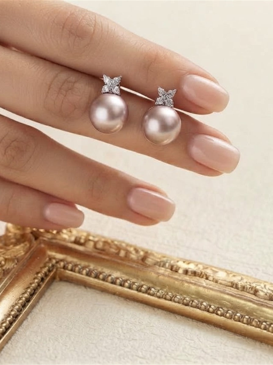 Pink pearl butterfly stud earrings held between the fingers above a gold frame